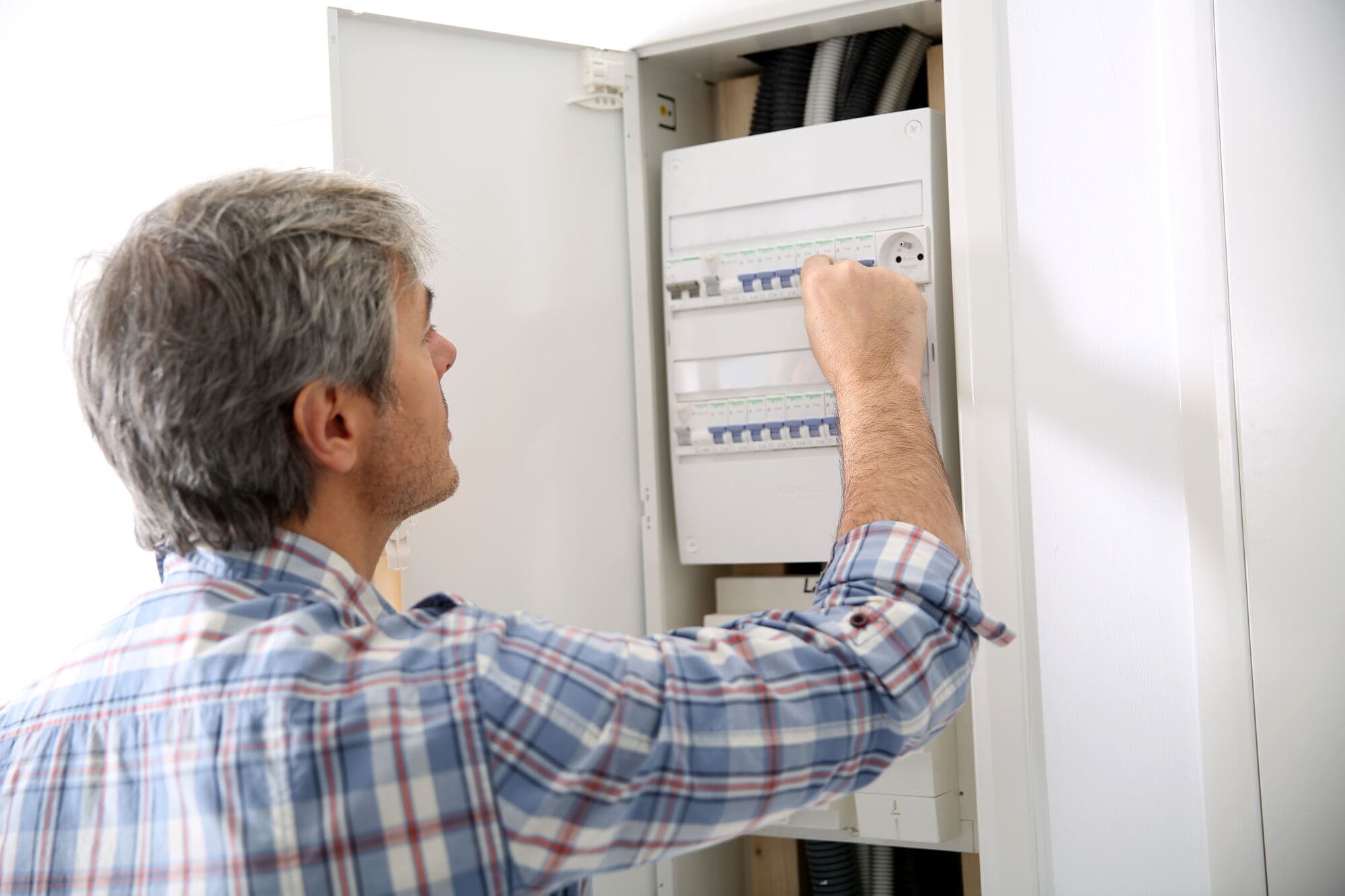 Elektriker i rutig skjorta arbetar i en öppen elcentral i ett bostadshus